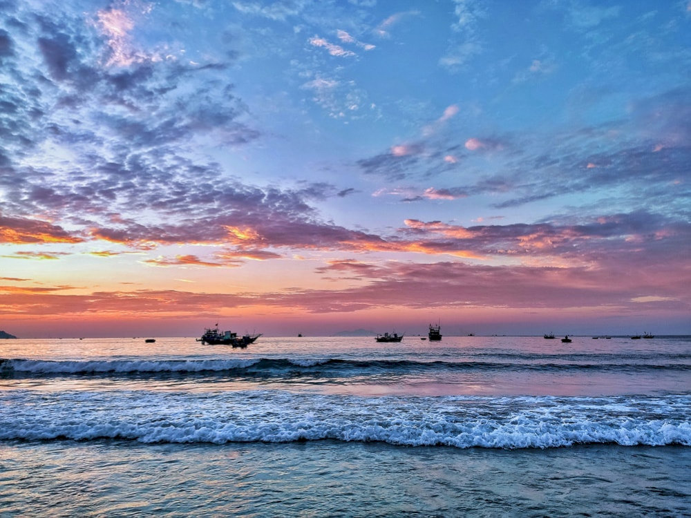 As the sun sets, fishing boats slowly make their way back to shore after a long day out at sea